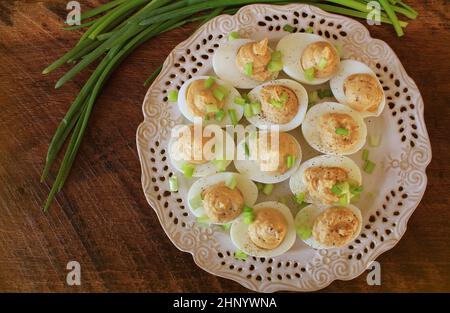Deviled eggs with cod livers with leek on white plate. Rustic wooden table . Stock Photo