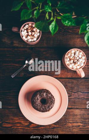 Stack of Homemade Chocolate Donuts and Mugs of Hot Chocolate with Marshmallow on Rustic Wooden Surface. View from Above Stock Photo
