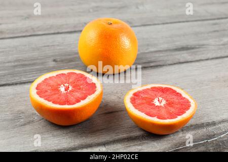 Pink grapefruit cut to half, with other whole citrus in background, placed on gray wood table. Stock Photo