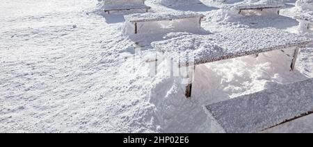Winter snow loadings banner. Sun shining on desks and benches completely covered under deep snowfall. Stock Photo