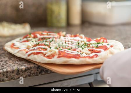 Pizza cook putting pizza in oven in a pizzeria, close up. Stock Photo