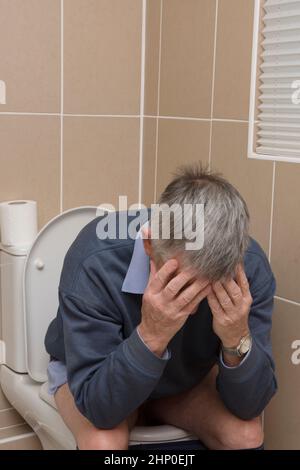 man sitting on toilet holding his head in his hands, diarrhoea or constipation Stock Photo