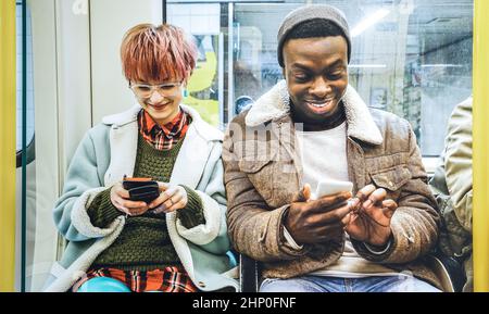 Multiracial hipster friends couple having fun with smartphone in subway train - Urban relationship concept with young people watching mobile phone in Stock Photo