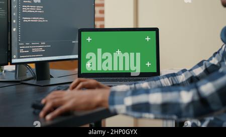 Closeup of laptop with green screen chroma key mockup and african american hands writing code on computer keyboard. Programer developing software in front of multiple screens running ai algorithm. Stock Photo