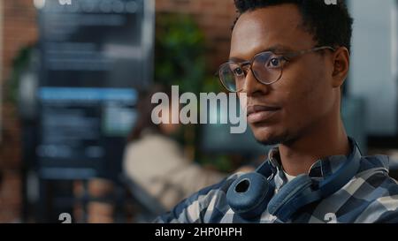 Closeup portrait of software engineer writing code fixing glasses and smiling sitting at desk. Database admin developing algorithms for artificial intelligence to innovate online cloud computing. Stock Photo
