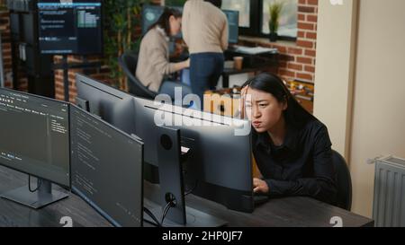 Portrait of asian programer focused on writing code encounters unexpected compiling error sitting at desk in software development office. Coder having system failure while creating algorithm. Stock Photo