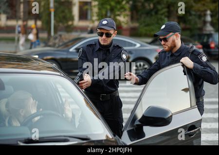 Police patrol with gun arrests female driver. Policemen in uniform protect the law, registration of an offense. Cops work on city street, order and ju Stock Photo
