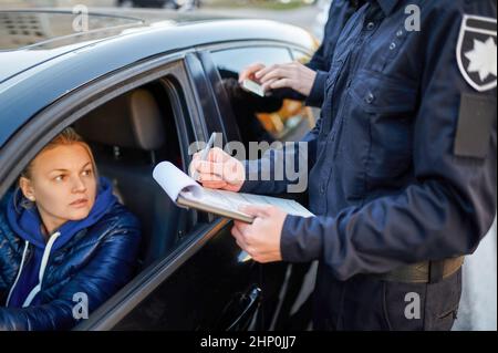 Police patrol checking driver's license of female driver. Policemen in uniform protect the law, registration of an offense. Cops work on city street, Stock Photo