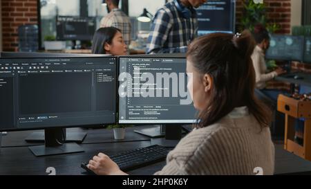 Software programer writing code in front of multiple computer screens displaying artificial intelligence algorithm. Developer coding database while colleagues doing online cloud computing. Stock Photo