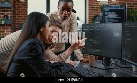 Programer pointing at computer screen explaining running code to coworkers brainstorming software ideas in freelance agency. Mixed team of software engineers collaborating on it group project. Stock Photo