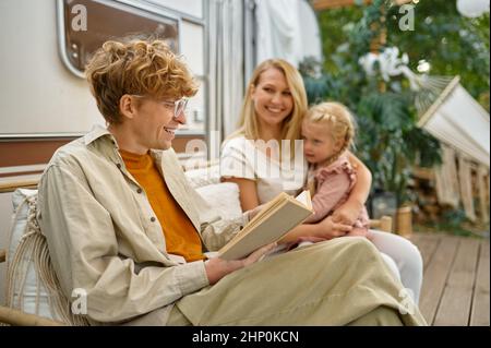 Funny family relaxing at the motorhome, summer camping. Parents with children travel in camp car, nature and forest on background. Campsite adventure, Stock Photo