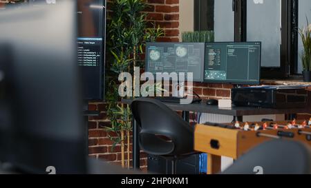 Desk with multiple computer monitors displaying neural network visualisation and artificial intelligence parsing code. Empty software developing agency office with servers cloud computing. Stock Photo