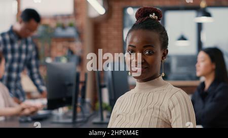 Portrait of smiling african american software developer looking at camera in artificial intelligence development agency. Confident programer posing next to colleagues working in big data office. Stock Photo