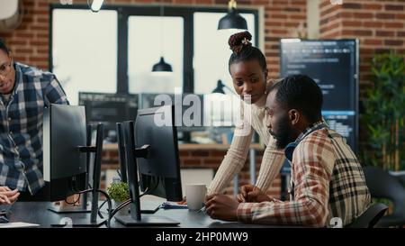 Mixed team of programmers brainstorming ideas for new cloud computing user interface looking at running code on computer screens. Developers collaborating on group project compiling algorithm. Stock Photo
