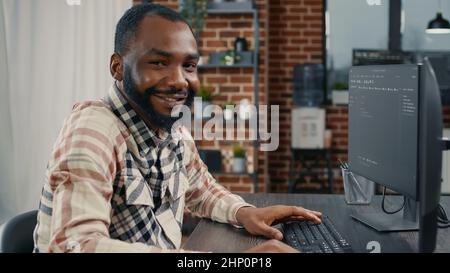 Software developer typing programming code on computer keyboard turning head and smiling while innovating online cloud computing. Casual programer sitting at desk writing code feeling confident. Stock Photo