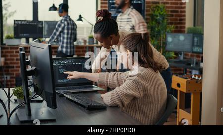 Two software coders analyzing source code looking for errors running on laptop screen while sitting at desk. Team of system engineers working on cyber security innovation in busy server room. Stock Photo