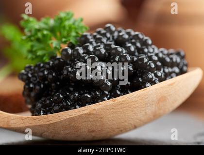 fresh grainy black paddlefish caviar in brown wooden spoon on a black background, close up Stock Photo