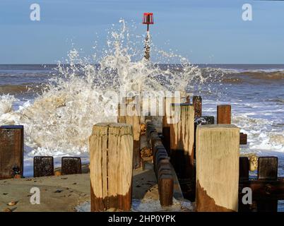 Waves breaking over wooden sea defences at Walcott, Norfolk during rough seas following a storm causing spray and sea foam. Stock Photo