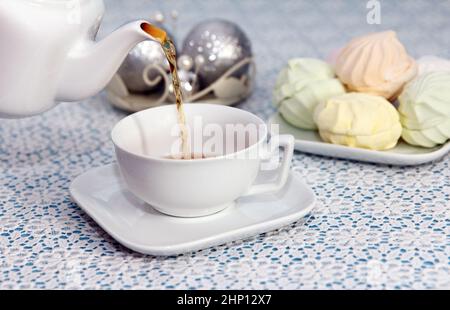Tea party time. Hostess pours tea into cups from the kettle, in a piece with delicious fresh marshmallows, on festive table Stock Photo