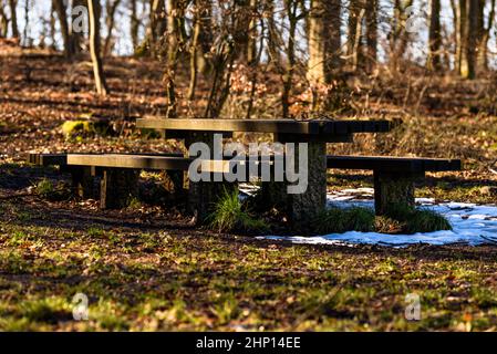 Rest area with benches and table with snow residue in front of forest Stock Photo