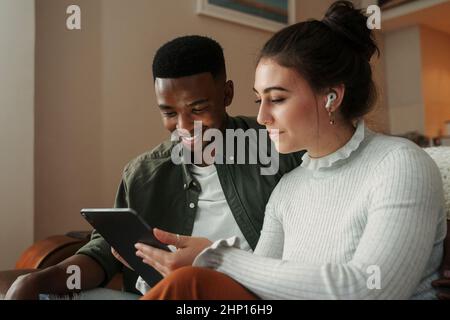 Biracial couple sitting on sofa scrolling on digital tablet  Stock Photo