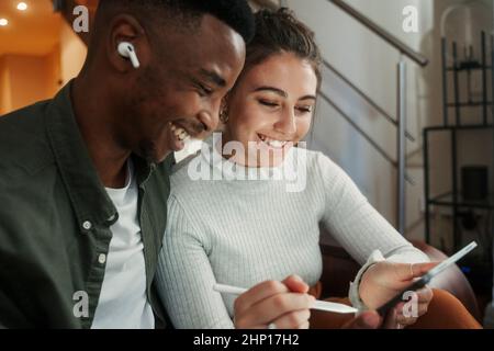 biracial couple sitting on sofa drawing with pen on digital tablet  Stock Photo