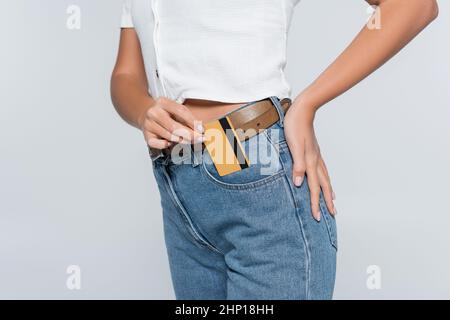 cropped view of young woman putting credit card with cashback in pocket on jeans isolated on grey Stock Photo