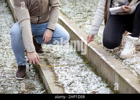 Unrecognizable young couple in casual upper garments sitting, making calculations using measuring tape , writing notes. Stock Photo