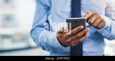 Taking a quick look at my social media. Cropped shot of an unrecognizable businessman standing alone in the office and using his cellphone to text. Stock Photo