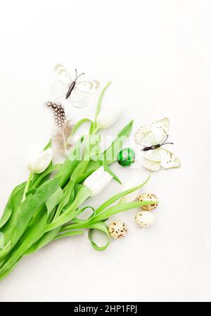 Spring Easter holiday white background with tulips, quail eggs, butterflies and feathers. Top view Stock Photo