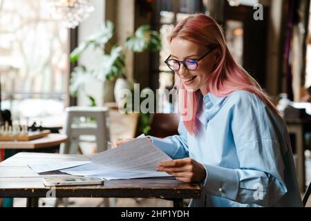 Young beautiful woman with pink hair doing paperwork while sitting in cafe Stock Photo