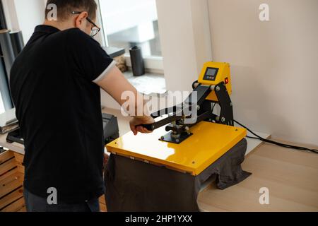 Man worker glasses back using heat thermal textile application transfer machine. Printing application art design T-shirt Stock Photo