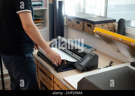 Cropped man worker side back using sticker cutting application vinyl film membrane sticker. Printing application design. Stock Photo