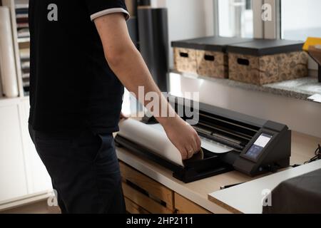 Cropped man worker side back using cutting carve application vinyl film membrane sticker. Printing application design. Stock Photo