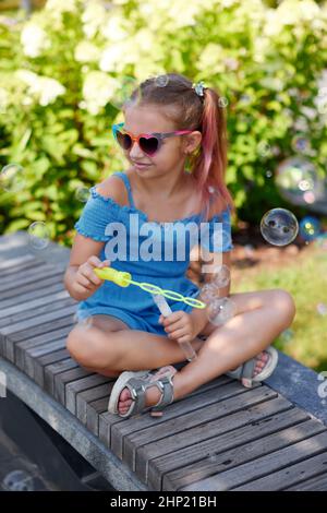 little child girl blowing soap bubbles in summer park. Stock Photo