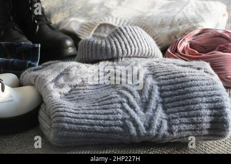 A set of fashionable winter women's clothing. Wool sweater, shoes, handbag, fur hat and gloves on white wooden background. Stock Photo