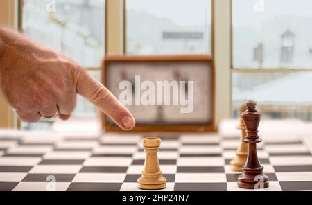 The hand and chessboard with figures and clock on blurred window background. Selective focus Stock Photo