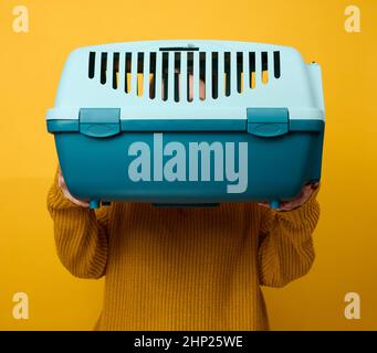 woman in brown sweater holding plastic pet carrier cage on yellow background Stock Photo