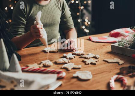 Merry Christmas, Happy New Year. A little small baby girl decorates cookies with protein white cream using culinary bag. Festive gingerbread cooking, Stock Photo
