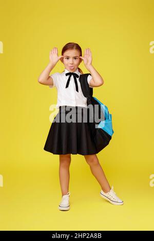 funny little schoolgirl with blue backpack isolated on yellow background. Stock Photo