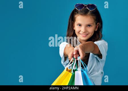 happy little caucasian child girl holds many shopping bags on blue background. focus on bags Stock Photo