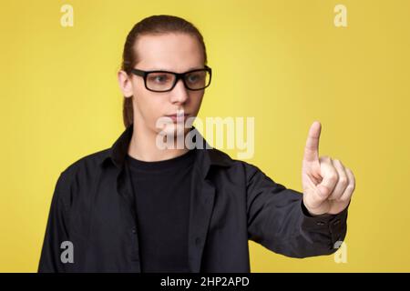 young man in glasses touching virtual screen on yellow background. focus on finger Stock Photo