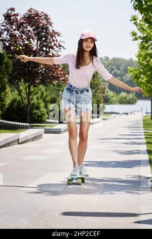 young beautiful skateboarder girl in cap riding on the skateboard in park Stock Photo