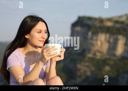 Asian woman looking away drinking coffee sitting in the mountain a sunny day Stock Photo