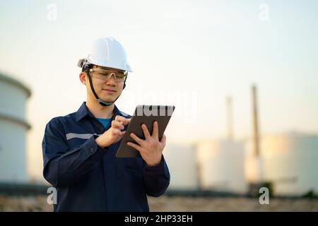 Asian engineer man are checking the maintenance of the oil refinery factory at evening via digital tablets. Stock Photo
