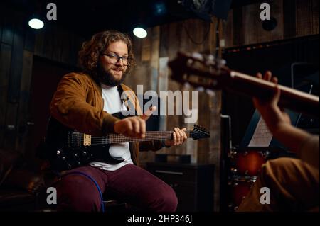 Musician teaching guy playing guitar at personal studio. Focus on tutor gesturing with index finger Stock Photo