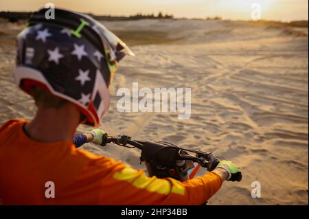 Motocross MX rider wearing protective helmet on motorcycle looking at sand road. View from shoulder Stock Photo