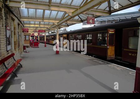 Heritage railway coaches from the steam era waiting with open doors for passengers at Keighley preserved railway platform with old fashioned signage Stock Photo