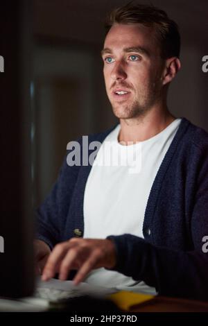 Working overtime. Cropped shot of a young man working late in his office. Stock Photo