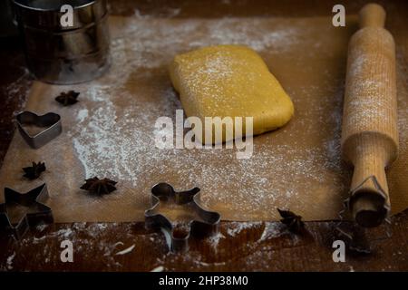 The dough lies on parchment next to a rolling pin and cookie cutters, flour is scattered everywhere, the photo is in dark colors. High quality photo Stock Photo